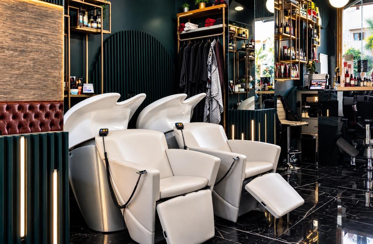 Deux fauteuils de lavage blancs avec bacs à shampoing, étagères dorées et mur cannelé vert